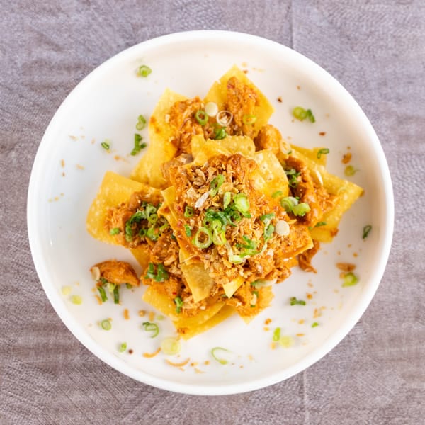 Crispy fried wontons topped with savory meat, fried garlic, and fresh green onions on a white plate.