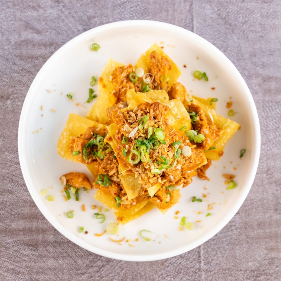 Crispy fried wontons topped with savory meat, fried garlic, and fresh green onions on a white plate.