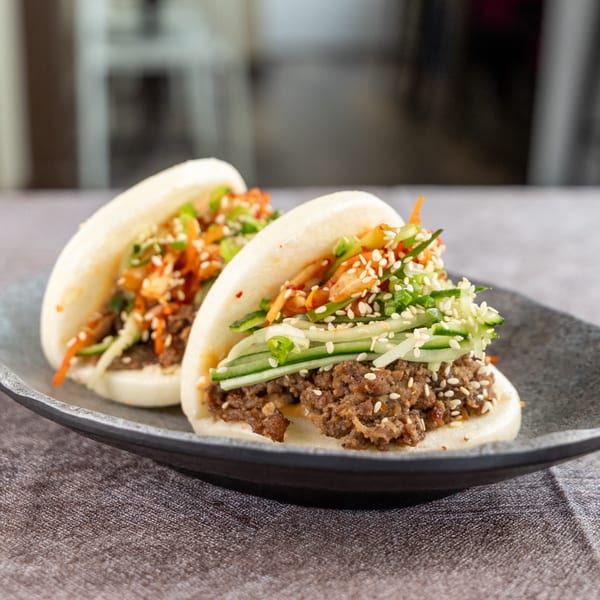 Two bao buns filled with ground meat, cucumber, kimchi, green onions, and sesame seeds.