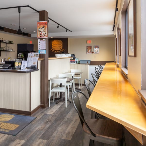 Interior of Bao & Beyond restaurant with a counter, dining tables, and a long bar by the window.