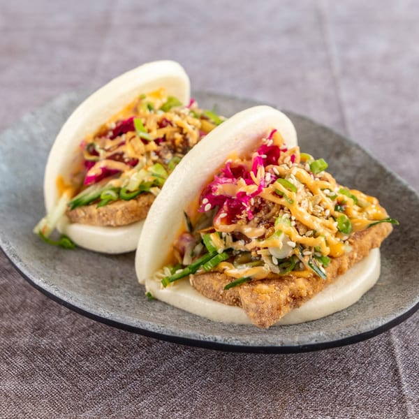 Two bao buns with crispy tofu, pickled cabbage, scallions, and a creamy orange sauce.