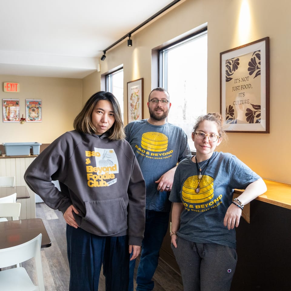 Three Bao & Beyond staff members, two women and one man, pose inside the restaurant.