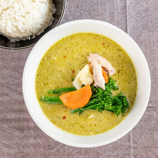 Green curry with chicken, broccoli, carrots, and cauliflower, served with a side of white rice.