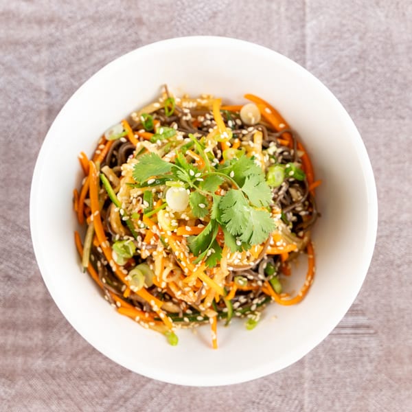 Overhead view of a soba noodle salad with carrots, scallions, sesame seeds, and cilantro.