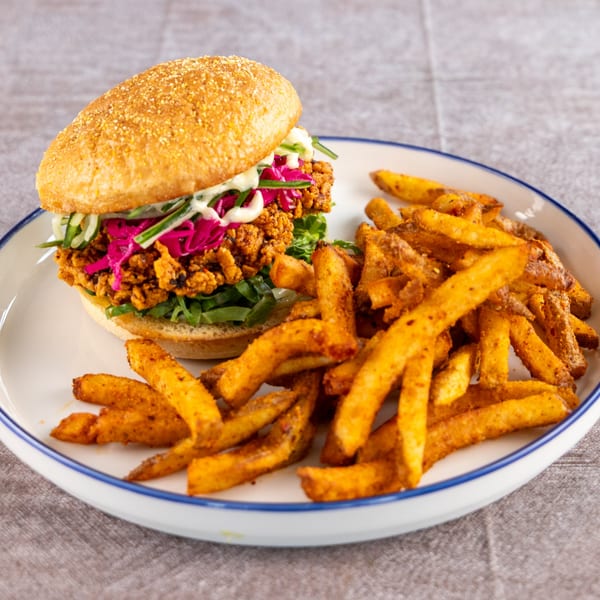 Crispy fried chicken burger with pickled red cabbage and fries on a white plate.