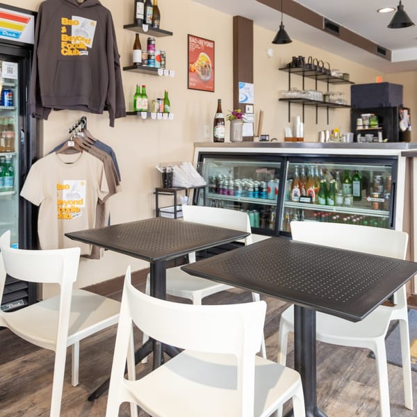 Interior of Bao & Beyond restaurant with tables, chairs, merchandise, and a beverage cooler.