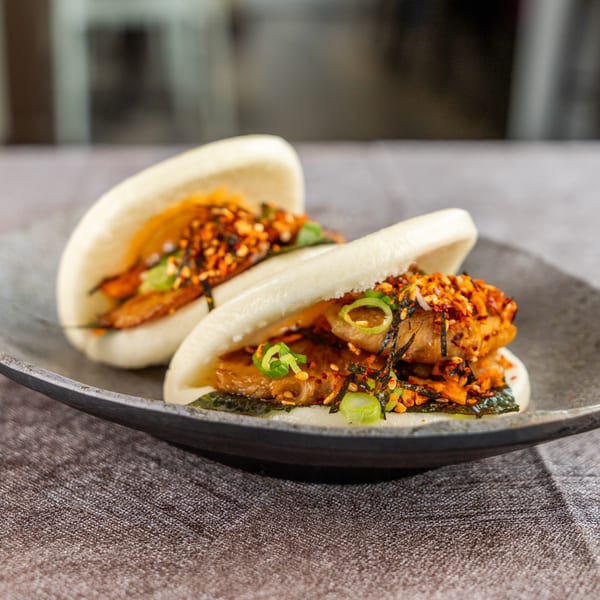 Two bao buns filled with meat, seaweed, and spices on a dark gray plate.