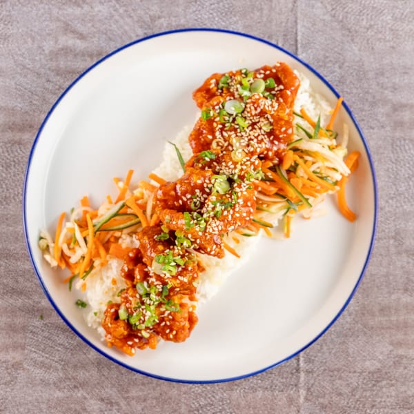 Sweet and sour chicken with rice and julienned vegetables, garnished with sesame seeds and scallions.