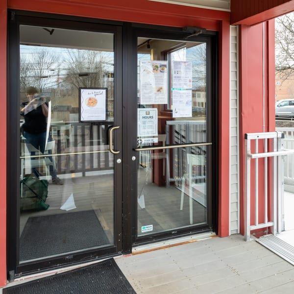 Restaurant entrance with glass doors, menus, hours, and a ramp leading to the patio.
