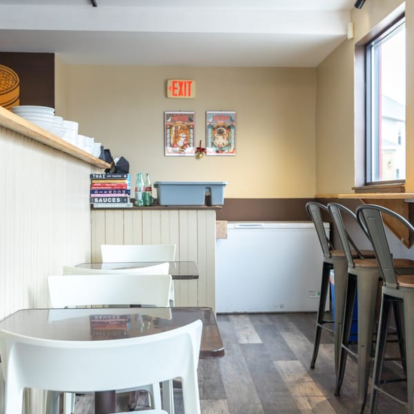Empty restaurant interior with white tables and chairs, bar stools, and an exit sign.