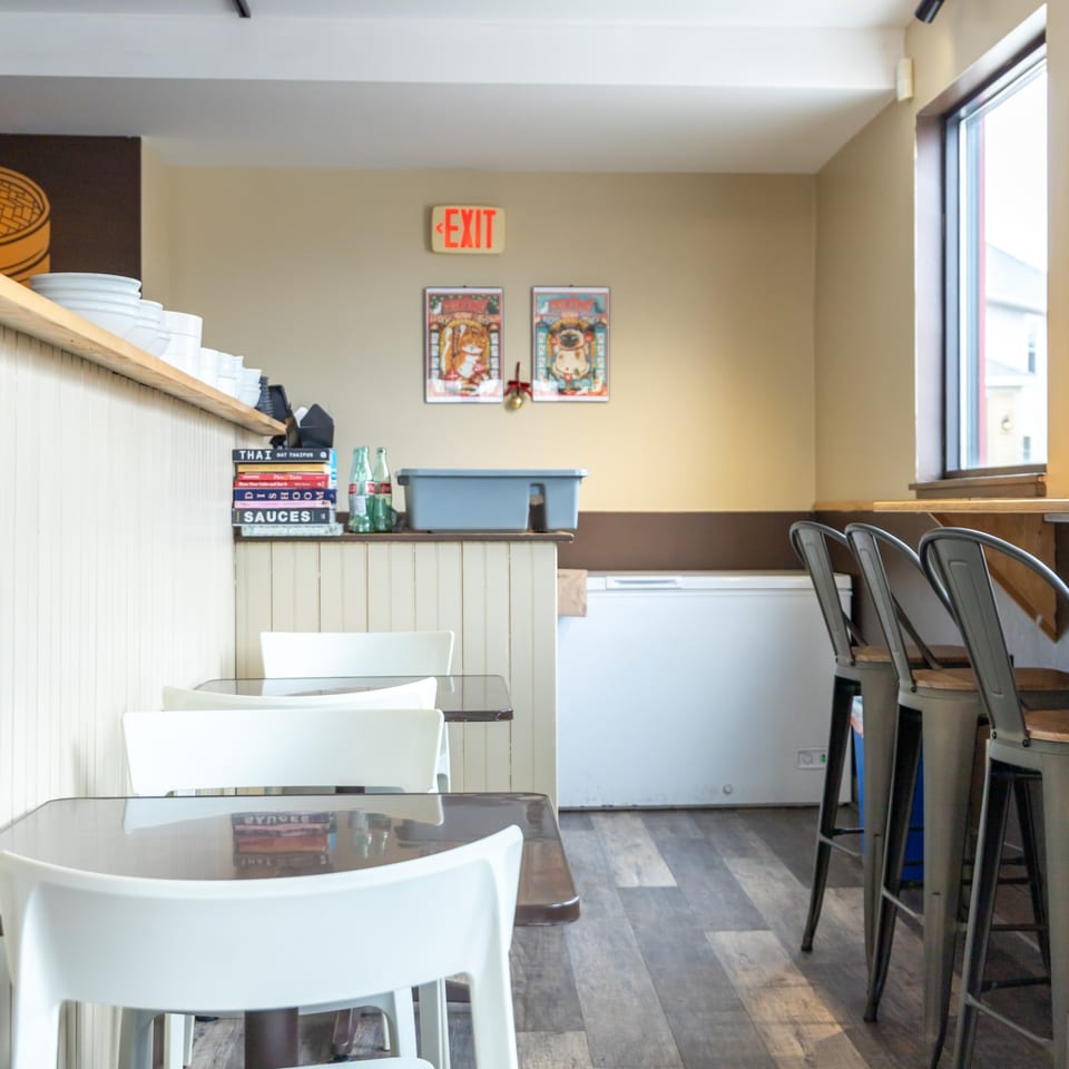 Empty restaurant interior with white tables and chairs, bar stools, and an exit sign.