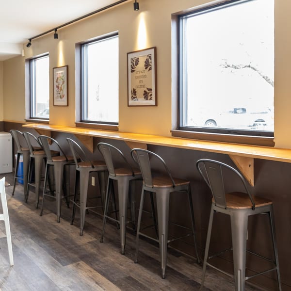A row of metal bar stools with wooden seats lines a window counter in a cafe.