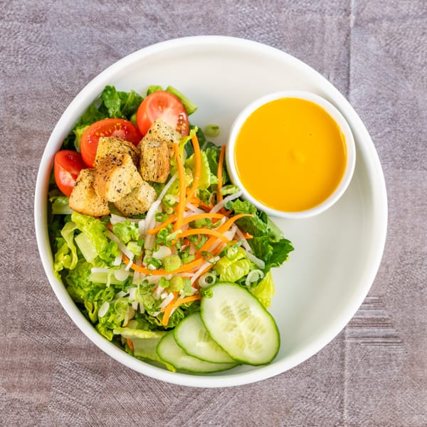 Fresh garden salad with lettuce, tomatoes, croutons, cucumbers, and a side of orange dressing.