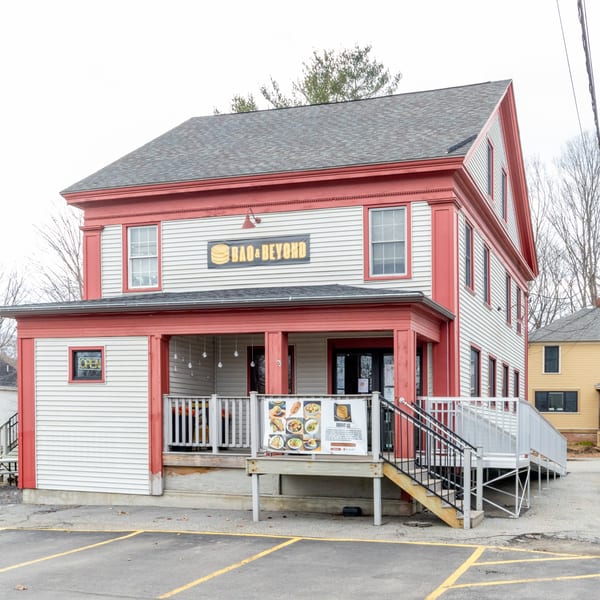 The Bao & Beyond restaurant, a two-story white building with red trim, features an outdoor patio.