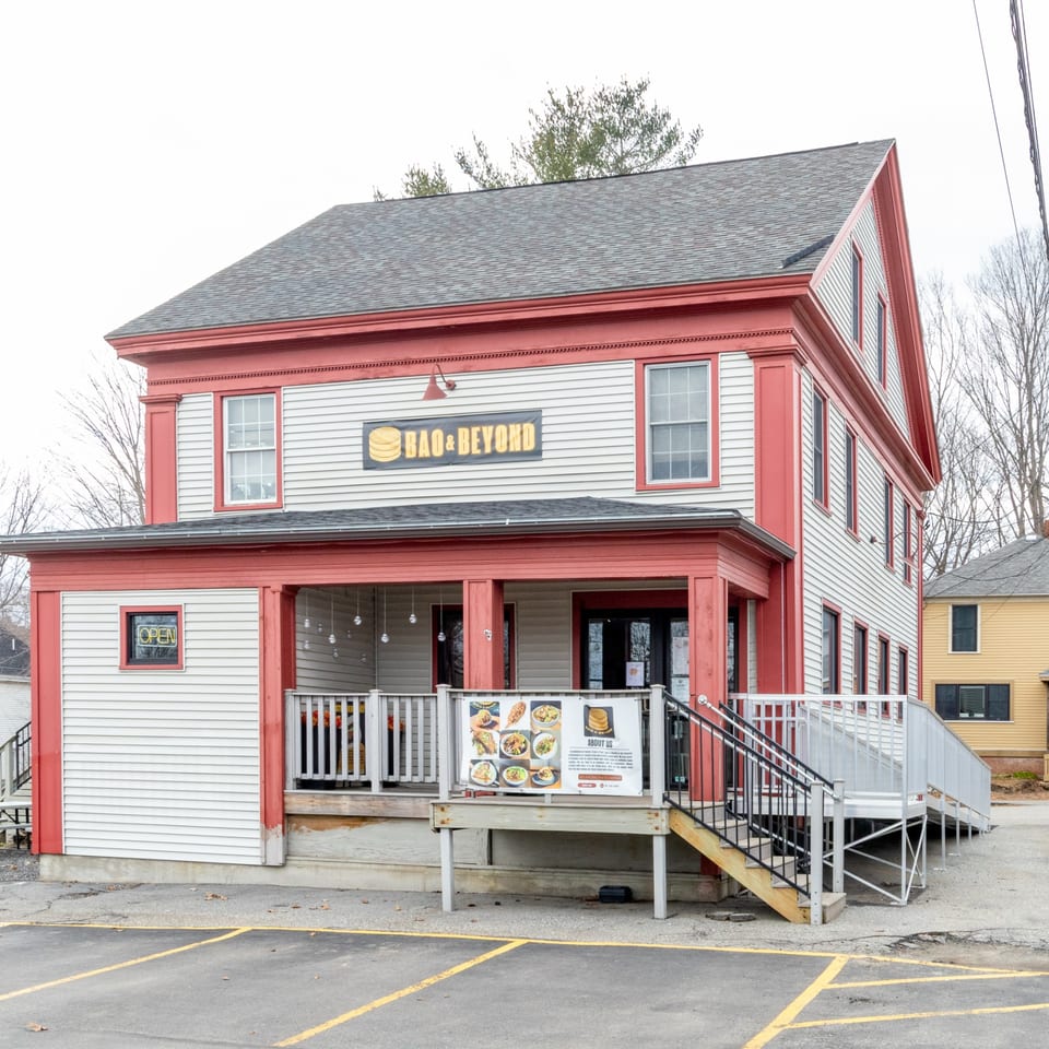 The Bao & Beyond restaurant, a two-story white building with red trim, features an outdoor patio.